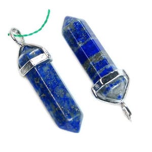 May include: Two blue lapis lazuli pendants with silver-colored metal caps and loops. The pendants are a deep blue color with gray and white marbling. A green string is attached to one pendant.