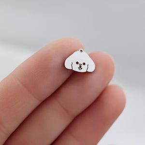 May include: A small, silver-colored charm in the shape of a dog's head. The charm has a rounded shape with a small loop at the top for attaching to a necklace or bracelet. The dog's face features small, round eyes and a smiling mouth.