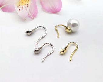 May include: Close-up of four earrings. Two are silver-colored, teardrop-shaped, and have a curved hook. The other two are gold-colored, with a teardrop shape and a curved hook. One gold earring has a large, white, round pearl attached.
