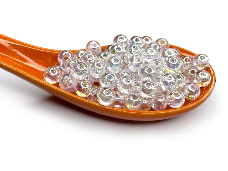 Peut inclure: Gros plan d'une petite cuill&egrave;re en c&eacute;ramique orange remplie de perles de verre transparentes et iris&eacute;es.