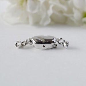 May include: Silver-toned clasp for a necklace or bracelet. The clasp is oval-shaped and has a smooth, polished finish.