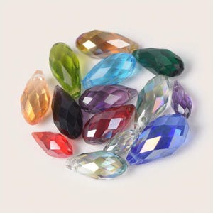 Pode incluir: Uma coleção de contas facetadas em forma de gota em várias cores, incluindo laranja, verde, azul, roxo e vermelho. As contas estão dispostas em um padrão circular, mostrando sua aparência brilhante e transparente. Adequado para fazer joias e projetos de artesanato.