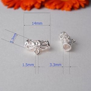 May include: Two silver-colored jewelry findings, each with a floral design and a small loop. One finding measures 0.55 inches wide and 0.21 inches high. The other finding is 0.13 inches wide. The findings are for jewelry making.