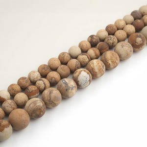 Könnte beinhalten: Nahaufnahme von Reihen natürlicher Steinperlen in verschiedenen Größen und Brauntönen, Beige und Creme. Die Perlen haben ein gesprenkeltes und marmoriertes Aussehen. Ideal für Schmuckherstellung oder Bastelprojekte.