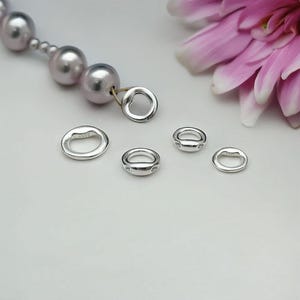 May include: Five silver jump rings of varying sizes. The rings are smooth and have a polished finish. The largest ring has a heart-shaped opening.