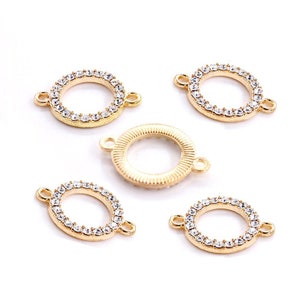 Op de afbeelding: Vijf goudkleurige metalen connector charms met heldere strass accenten. Twee van de charms zijn rond, twee zijn ovaal en &eacute;&eacute;n is rond en heeft een textuur.