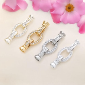 May include: Four silver and gold tone metal clasps with clear crystal accents. Each clasp features an oval-shaped design with a decorative, detailed center.