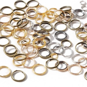 Puede incluir: Surtido de anillas de salto doradas, plateadas y bronce. Las anillas de salto son de varios tamaños y están esparcidas sobre un fondo blanco.