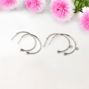 Peut inclure: Deux paires de boucles d'oreilles créoles argentées avec une petite boule au bas de chaque créole. Une paire a une petite boucle en haut de la créole.