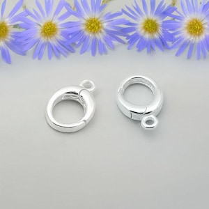 May include: Two silver-toned metal clasps for jewelry making. Each clasp has a round shape with a spring-loaded opening.