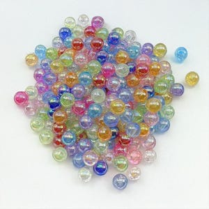 May include: A large pile of iridescent rainbow coloured glass beads. The beads are round and have a smooth, shiny finish.