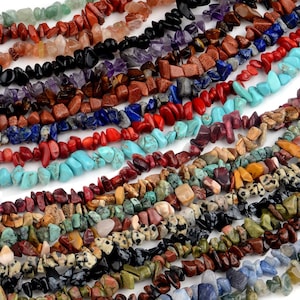 May include: Assortment of colorful gemstone chip beads, including turquoise, red coral, amethyst, lapis lazuli, and tiger's eye. The beads are irregular in shape and size, and are strung on a white background.
