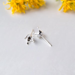 Puede incluir: Dos engastes de pendientes de plata con garras para sujetar una piedra preciosa. Los engastes están sobre un fondo blanco.