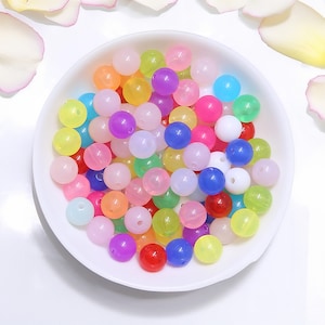 May include: A bowl filled with colorful translucent round beads. The beads are in various shades of pink, blue, green, yellow, orange, and purple.