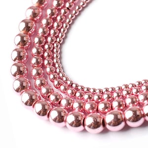 May include: A set of four strands of pink metallic beads, each strand with a different size of beads. The beads are round and have a shiny finish.