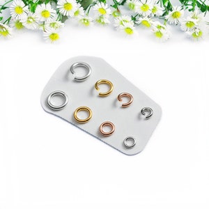 May include: A set of seven jump rings in different sizes and colors, including silver, gold, and rose gold. The rings are displayed on a white card.