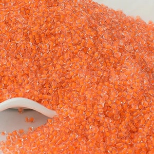 May include: A close-up of a pile of small, clear orange beads. The beads are round and have a slight shimmer to them.