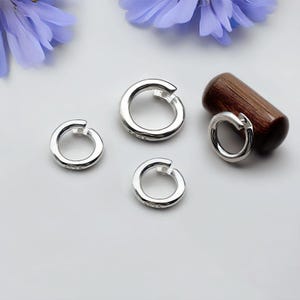 Peut inclure: Trois anneaux de saut en argent de différentes tailles, le plus petit à gauche et le plus grand à droite. Les anneaux sont sur une surface blanche.