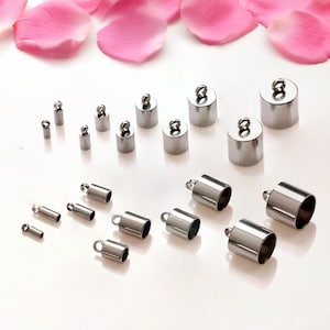 Puede incluir: Surtido de tapones de extremo de metal plateado para la elaboración de joyas. Los tapones de extremo son de varios tamaños y formas, incluyendo redondos, cuadrados y rectangulares. Algunos tapones de extremo tienen un bucle en la parte superior para sujetar una cuerda o cadena.