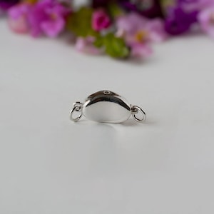 May include: Silver-toned clasp for a necklace or bracelet. The clasp is shaped like a small, smooth oval with a small hole in the centre.