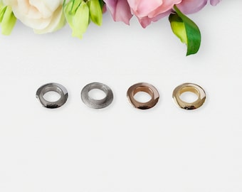 May include: Four metal eyelets in different finishes: silver, nickel, rose gold, and gold. The eyelets are arranged in a row on a white background.