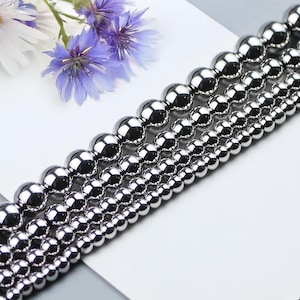 May include: A set of silver metal beads of varying sizes. The beads are round and smooth, and they are arranged in rows from largest to smallest.