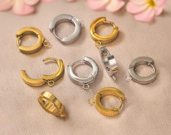 May include: A collection of eight gold and silver hoop earrings with a hinged closure. The earrings are arranged on a light brown surface.