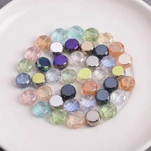May include: A collection of colorful, faceted glass beads in various shades of blue, pink, yellow, and iridescent hues. The beads are round and have a reflective, shiny surface, perfect for jewelry making or crafting projects.
