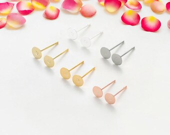 May include: Six pairs of earring findings in different metal finishes: gold, silver, and rose gold. Each pair features a round, flat disc with a small hole in the center and a straight post.