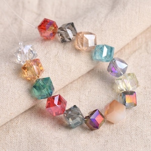 May include: A strand of faceted, cube-shaped beads in various colors, including red, gray, orange, green, and iridescent. The beads are strung on a thin, clear cord, creating a colorful and eye-catching design. The beads are approximately 0.5 inches in size.