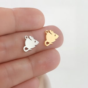 Op de afbeelding: Twee kleine muisvormige bedels. De ene bedel is zilverkleurig, de andere goudkleurig. Elke bedel heeft een kleine lus aan de bovenkant om aan sieraden te bevestigen. De metalen bedels hebben een gladde afwerking.