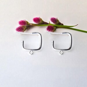 May include: Two silver square earring hoops with a small loop at the bottom. The hoops are about 1 inch in diameter.