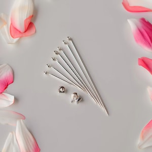 Pode incluir: Um conjunto de oito pinos de brinco prateados com uma pedra transparente no topo. Os pinos estão dispostos em forma de leque sobre uma superfície branca. Inclui dois fechos de brinco prateados.