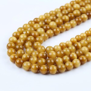 May include: Close-up of strands of golden-brown, polished beads. The beads are round with a glossy finish, suggesting they are for jewellery. The beads are uniform in size and shape, creating a smooth texture. Each bead is approximately 0.8 cm in diameter.