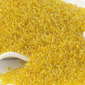 May include: A large quantity of small, round, yellow glass beads. The beads have a slight iridescent sheen.