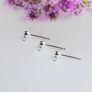 Puede incluir: Tres postes de pendientes de plata con pequeñas bolas redondas en la parte superior y un bucle en la parte inferior. Los postes son de diferentes longitudes.