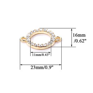 Op de afbeelding: Gouden metalen connector met een cirkel van heldere strass steentjes. De connector meet 16 mm in diameter en 23 mm in lengte.