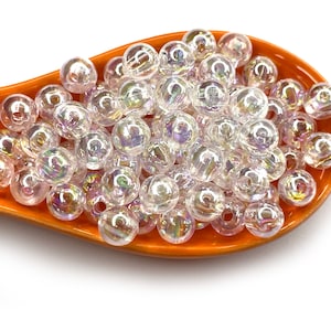 Peut inclure: Gros plan sur un tas de perles en plastique transparentes iris&eacute;es dans une cuill&egrave;re orange. Les perles sont rondes et ont un l&eacute;ger &eacute;clat.
