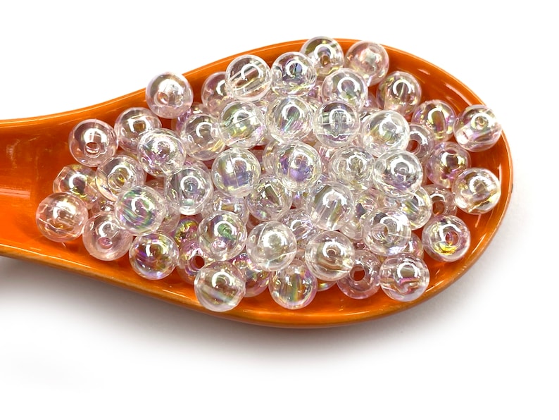 Peut inclure: Gros plan sur un tas de perles en plastique transparentes iris&eacute;es dans une cuill&egrave;re orange. Les perles sont rondes et ont un l&eacute;ger &eacute;clat.