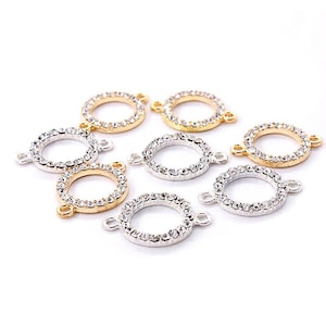 Op de afbeelding: Een groep van acht ronde connector-bedels in goud en zilver met heldere strass-accenten. Elke bedel heeft twee springringen om aan sieraden te bevestigen.