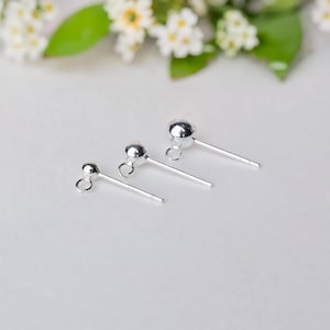 Può includere: Tre perni per orecchini in argento di diverse dimensioni con un anello nella parte superiore. I perni sono disposti in ordine di dimensione, con il più piccolo a sinistra e il più grande a destra.