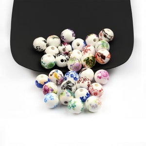 Peut inclure: Un ensemble de perles en céramique blanche avec des motifs floraux colorés. Les perles sont rondes et ont une finition lisse et brillante.