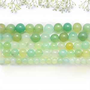 Puede incluir: Cadenas de cuentas de piedras preciosas verdes en varios tonos, sobre un fondo blanco. Las cuentas son redondas y pulidas, con un acabado brillante. La imagen está bien iluminada, mostrando el color y la textura de las cuentas. Medidas en centímetros.