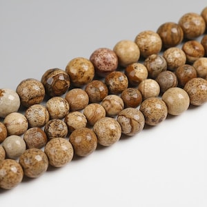 Könnte beinhalten: Nahaufnahme einer Kette aus natürlichen Edelsteinperlen. Die Perlen sind rund, mit einer Mischung aus Beige-, Braun- und Cremefarben. Die Perlen haben ein gesprenkeltes Muster und variieren in der Größe, wodurch eine natürliche, erdige Ästhetik entsteht.