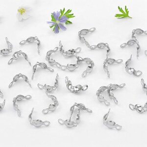 May include: A collection of silver-toned metal bead caps, designed to finish off jewellery projects. The caps have a rounded shape with a small loop on each side.