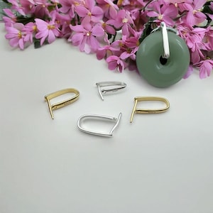 May include: Four silver and gold jump rings, each with a small loop on one side and a larger loop on the other. The rings are arranged on a white surface. The rings are used for jewellery making.