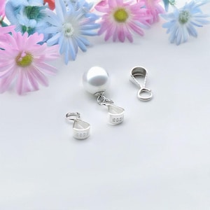 Puede incluir: Un colgante de perla blanca con un cierre de plata. El colgante está unido a una cadena de plata. Hay dos cierres de plata adicionales.