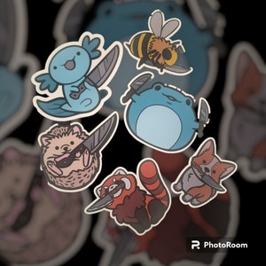 May include: A set of seven colorful stickers featuring various animals holding knives. The animals include a frog, a red panda, a hedgehog, a bee, an axolotl, and a corgi.