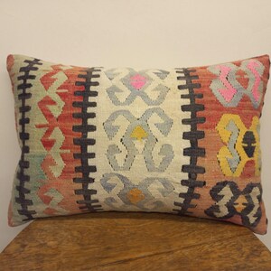 May include: A rectangular pillow with a colorful geometric pattern in shades of red, blue, yellow, and white. The pillow has a black border and is made of a woven fabric.