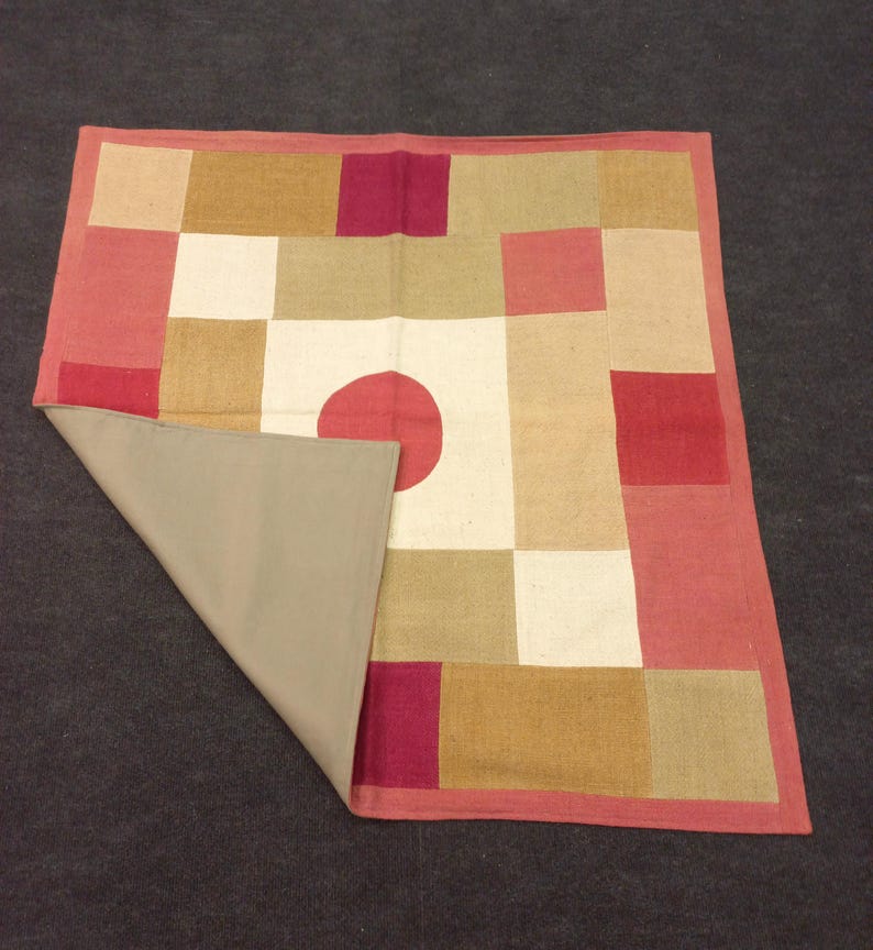 Może przedstawiać: Kwadratowy dywan w stylu patchwork z czerwonym kołem w środku. Dywan wykonany jest z tkanin w r&oacute;żnych kolorach, w tym czerwonym, brązowym i białym.